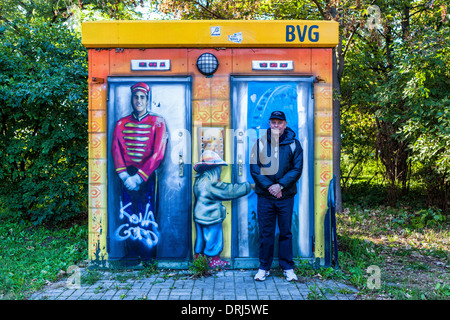 Senior woman imitiert Pose des street-Art-Begleiter auf WC außerhalb der S-Bahn-Bahnhof, Plånterwald, Treptow-Kopernick, Berlin Stockfoto