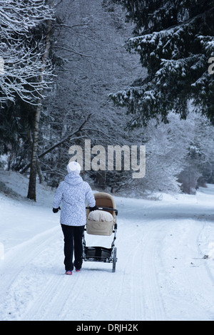 Eine Frau schiebt einen Kinderwagen oder Buggy in einem verschneiten Wald Stockfoto