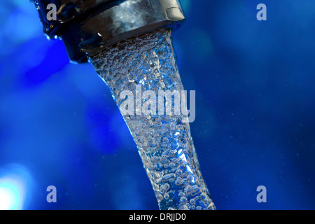 Wasser fließt aus einem Wasserhahn auf blauem Hintergrund Stockfoto