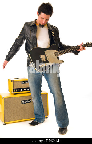 Ein Rockmusiker, e-Gitarre zu spielen, trägt er eine Lederjacke und Bluejeans. Hinten sind gelbe gestapelten Verstärker. Stockfoto