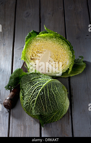 Halbierte Savoy (Brassica Oleracea Convar. Capitata var. Sabauda L.) und antiken Wiegemesser auf grauem Holztisch Stockfoto