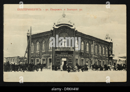 Toporishchev Lebensmittelgeschäft und Shustov Cognac-Geschäft in Pokrovsky Prospekt Avenue in Jekaterinburg, Russisches Reich. Schwarz-Weiß-Vintage-Fotografie des russischen Fotografen Nikolai Vwedensky datiert vom Anfang des 20. Jahrhunderts, ausgestellt in der russischen Vintage-Postkarte von M.S. Semkov, Jekaterinburg. Text auf Russisch: Jekaterinburg. Conner von Pokrovsky Prospekt Avenue und Zlatoustovskaya Straße. Winterszene. Mit freundlicher Genehmigung der Azoor Postcard Collection. Stockfoto