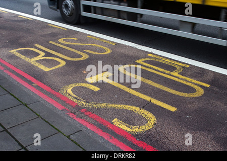 Die Worte "Bus Stop" gemalt auf einer Straße in London, leuchtend gelb mit einer roten Doppellinie Straße Markierung entlang. Stockfoto