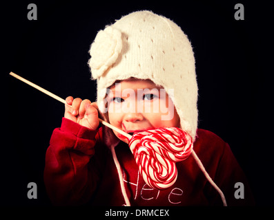 Schöne Babymädchen Essen eine herzförmige Süßigkeiten auf schwarzem Hintergrund Stockfoto