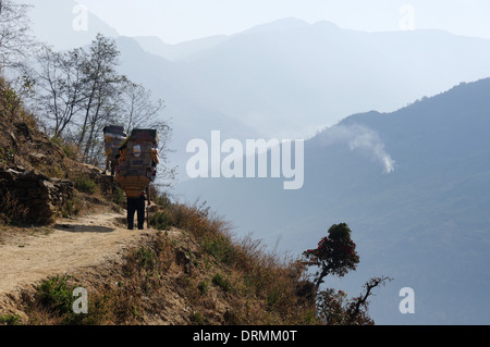 Ein Sherpa tragen eine schwere Last auf einem Bergpfad in Nepal Stockfoto