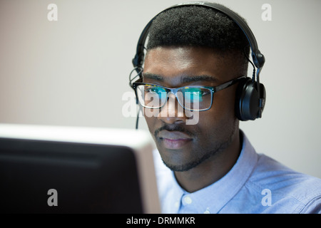 junger schwarzer Mann mit Kopfhörern im Büro am Computer arbeiten Stockfoto