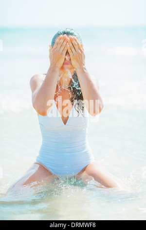 Junge Frau im Badeanzug waschen Gesicht mit Meerwasser Stockfoto