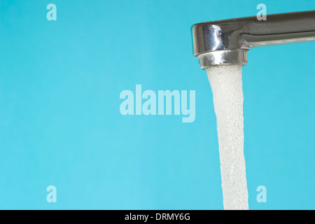 Wasser fließt aus einem Wasserhahn auf blauem Hintergrund Stockfoto