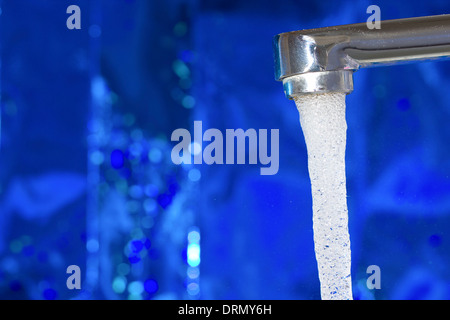 Wasser fließt aus einem Wasserhahn auf blauem Hintergrund Stockfoto