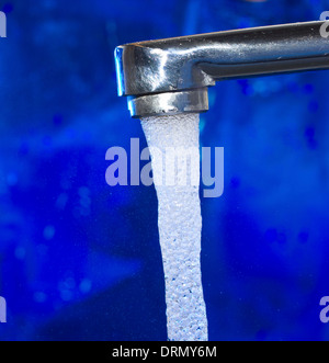 Wasser fließt aus einem Wasserhahn auf blauem Hintergrund Stockfoto