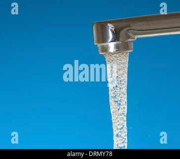 Wasser fließt aus einem Wasserhahn auf blauem Hintergrund Stockfoto