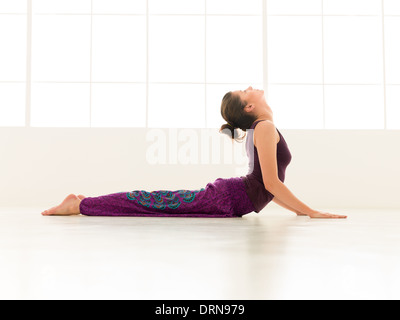 junge Frau schwer Yogastellung, Ganzkörper-Seitenansicht, bunt gekleidet demonstrieren lichtstärkeren Fenster backgrond Stockfoto