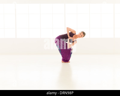 junge Frau schwer Yoga-Pose, bunt gekleidet demonstrieren lichtstärkeren Fensterhintergrund Stockfoto