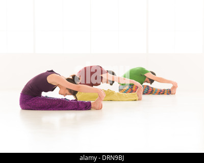 Drei junge Menschen eine Frau und zwei Männer üben Yoga Klasse Hintergrundfenster bunt Stockfoto