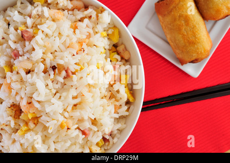 Nahaufnahme von einer Schüssel mit appetitlichen Chinesisch gebratener Reis und einige Frühlingsrollen in einer Platte auf einem gedeckten Tisch Stockfoto