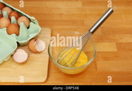 Schlagen von Eiern, Schüssel Eiern in einem Glas mischen mit einem Schneebesen auf einer hölzernen Küchenarbeitsplatte Stockfoto