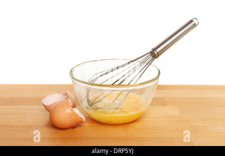 Eiern mit einem Schneebesen in einem Glas Schüssel auf einer Küchenarbeitsplatte vor einem weißen Hintergrund geknackt Stockfoto