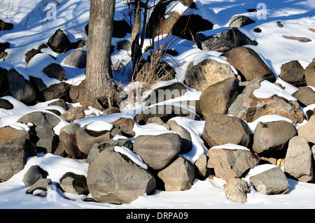 Verschneite Wellenbrecher Felsbrocken entlang Fluss Küste Stockfoto