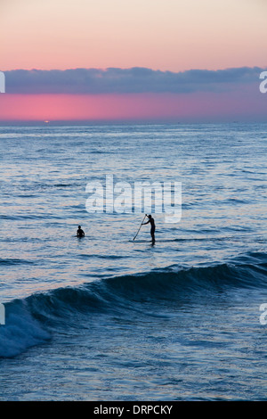 Ein Surfer und Paddler Boarder die Wellen in den Sonnenuntergang reiten. Stockfoto