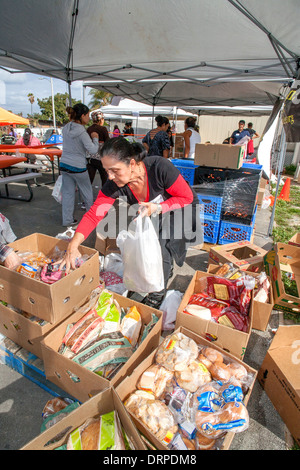 Hispanic Hausfrau wählt freie gespendeten Backwaren aus einer Charity-Website in einem Slum von Stanton, CA. Stockfoto