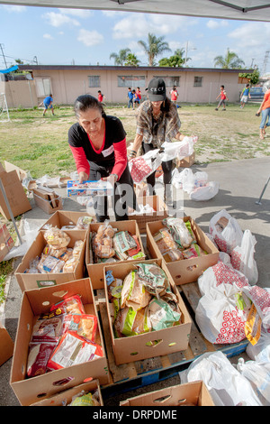 Hispanic Hausfrau wählt freie gespendeten Backwaren aus einer Charity-Website in einem Slum von Stanton, CA. Hinweis Freiwilligen Auspacken Lebensmitteln auf der rechten Seite. Stockfoto