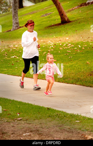 Ein kleines Mädchen läuft durch einen Park in Costa Mesa, Kalifornien, als ihre Großmutter ihr folgt. Stockfoto