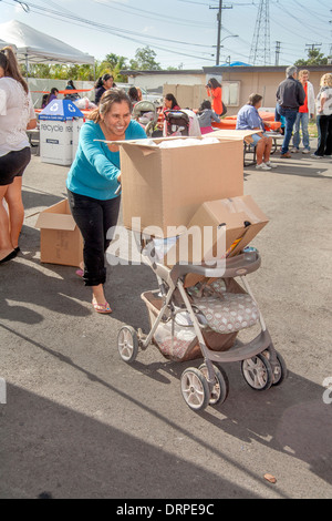 Hispanic Hausfrau verwendet einen Kinderwagen, um schwere Kisten von gespendeten Lebensmitteln aus einer Charity-Website in einem Slum von Stanton, CA zu tragen. Stockfoto