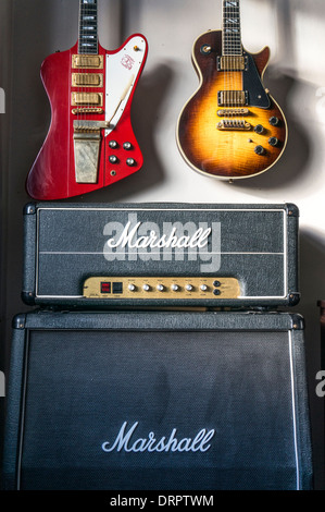 Hängende USA Gitarren über britische Marshall Verstärker und Lautsprecherbox: Gibson Firebird VII und Gibson Les Paul 25/50 Jubiläum Modell. Stockfoto