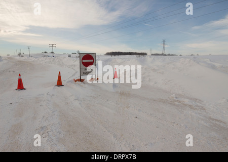 Ein Straßenschild Verschluss blockiert eine Fahrbahn nach Fahrzeugen im Wind geblasen, Winterschnee & schweren Winterbedingungen Blizzard verfangen Stockfoto