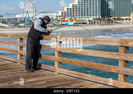 Fischer fängt einen Fisch auf dem Daytona Beach Fishing Pier mit dem öffentlichen Strand und Freizeitpark über sichtbar. Stockfoto