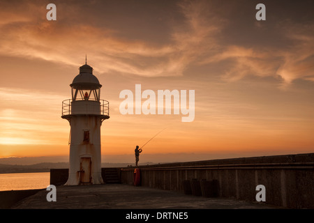 Leuchtturm und Mole in der Küstenfischerei Hafen von Brixham, South Devon mit einem Vergnügen Fischer bei Sonnenuntergang aufgenommen. Stockfoto