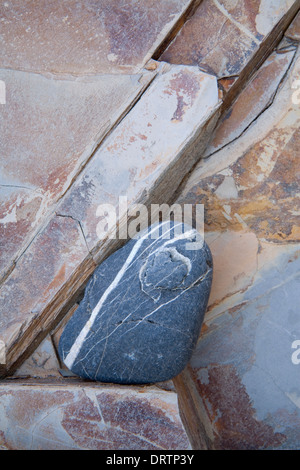 Ein blauen Stein mit weißer Maserung ist eingekeilt in die Ritzen der roten farbigen Schiefer Felsen in den Klippen am Dollar Cove, Cornwall, Englan Stockfoto