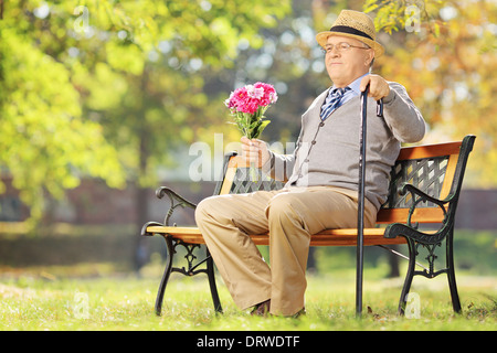 Ältere Gentleman mit Blumenstrauß sitzt auf einer Holzbank in einem park Stockfoto