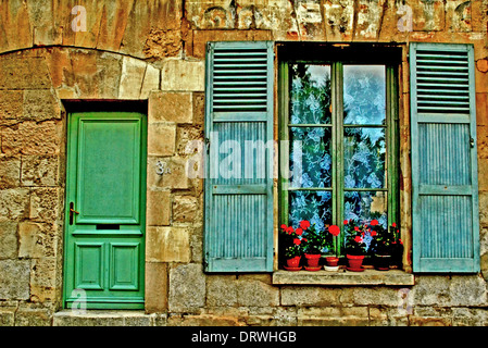 Aufbau der Fassade mit einem Fenster mit blauen Fensterläden und roten Geranien und einem grünen Holztür Stockfoto
