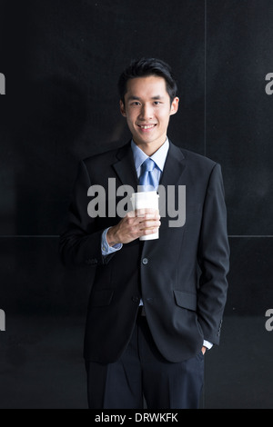 Chinesischer Geschäftsmann stützte sich auf eine schwarze Wand. Hübscher Junge chinesische Geschäftsmann eine schwarze Wand gelehnt. Stockfoto
