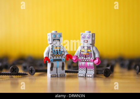 Männliche und weibliche Spielzeug Lego Roboter umgeben von Schrauben grau. Gelber Hintergrund, Holzboden Stockfoto