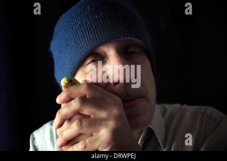 Lunatic Mann mit Hut hält einen Wellensittich Stockfoto