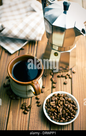 Kaffee mit Kaffeebohnen und Kaffeemaschine auf Holztisch Stockfoto