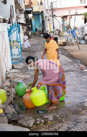 Indische Frauen Kunststoff-Töpfe mit Wasser aus einem Standrohr in einem indischen Dorf Straße zu füllen. Andhra Pradesh, Indien Stockfoto