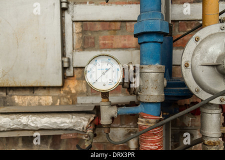 Rostige Manometer angeschlossen an Rohren mit Wand hinter Stockfoto