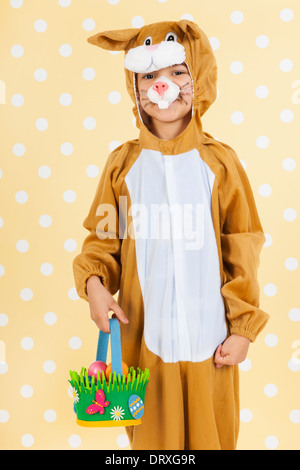 Kind verkleidet als Ostern Hase mit Korb Eiern auf gelben gestrichelten Hintergrund Stockfoto