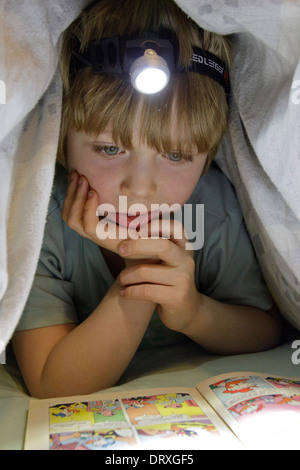 kleiner Junge mit einer Stirnlampe lesen unter seiner Bettdecke Stockfoto