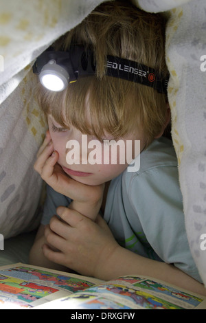 kleiner Junge mit einer Stirnlampe lesen unter seiner Bettdecke Stockfoto