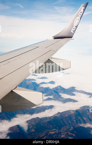 Schuss aus Flugzeugfenster, flyniki.com Logo auf Flugzeugflügel, mit blauen Wolkenhimmel und Alpen Berge im Hintergrund zeigen Stockfoto
