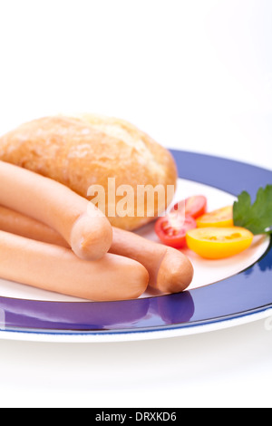 Drei kalt geräucherte Würstchen oder Wiener Würstchen serviert auf einem Teller mit einem Sprung in eine kleine Schüssel geben und in Scheiben geschnittenen Kirschtomaten auf ein weißes Studio-Hintergrund Stockfoto