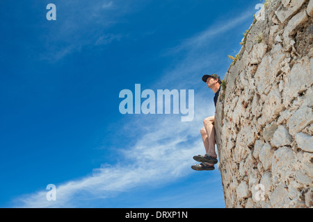 Junger Mann sitzt auf dem Rand der Steinmauer und in der Ferne suchen. Stockfoto