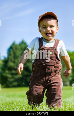 Junge Junge Kleinkind in Overall und Mütze in den Rasen laufen. Stockfoto