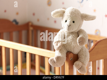 Kuschelige Schafe sitzt auf einem Kinderbett. Stockfoto