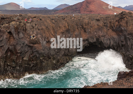 Touristen auf eine Aussichtsplattform mit einer großen Welle stürzt in einen See in der Höhle Klippen Los Hervideros Lanzarote Kanarische Inseln Stockfoto