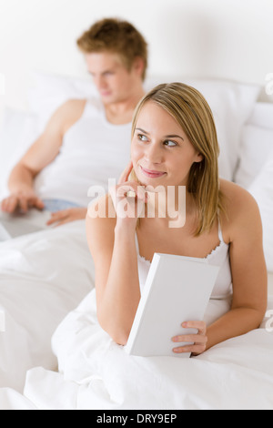 Nachdenkliche Frau mit Buch im Bett Stockfoto